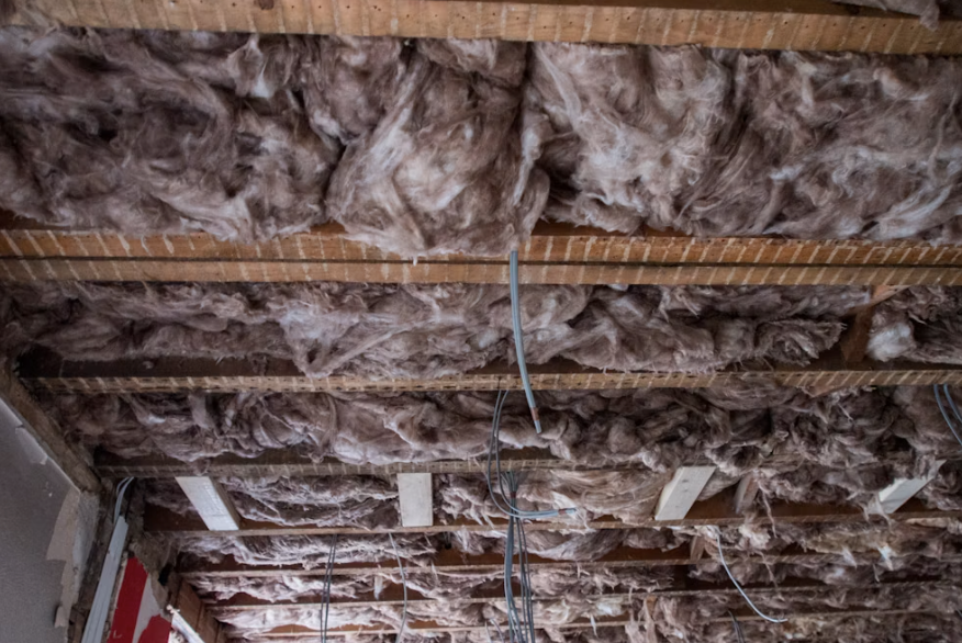 Aged mineral wool insulation between floor joists in a stripped building with old wiring.