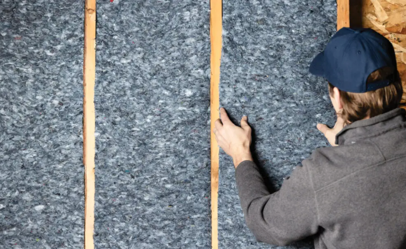 Installer fitting recycled denim insulation batts between wood studs.