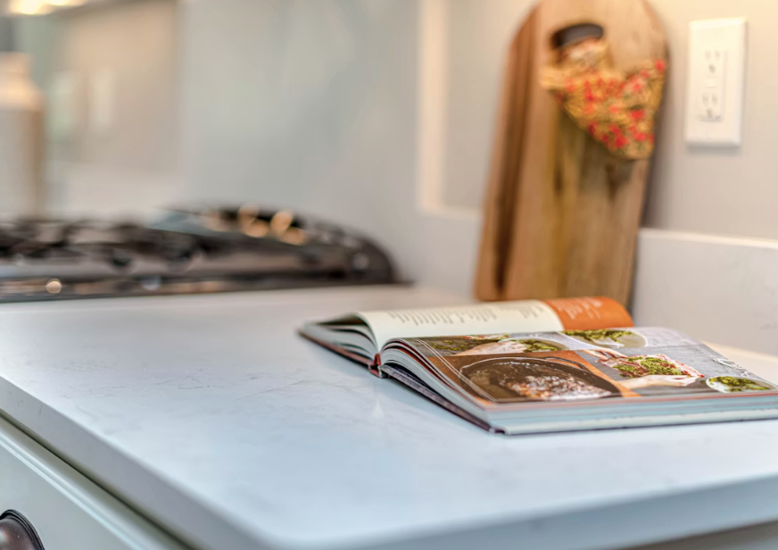 Open cookbook and a wooden cutting board on a light kitchen countertop.