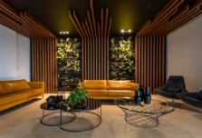 Commercial lounge, tan leather sofas, timber slat walls and ceiling, two planted living wall panels, stone floor.