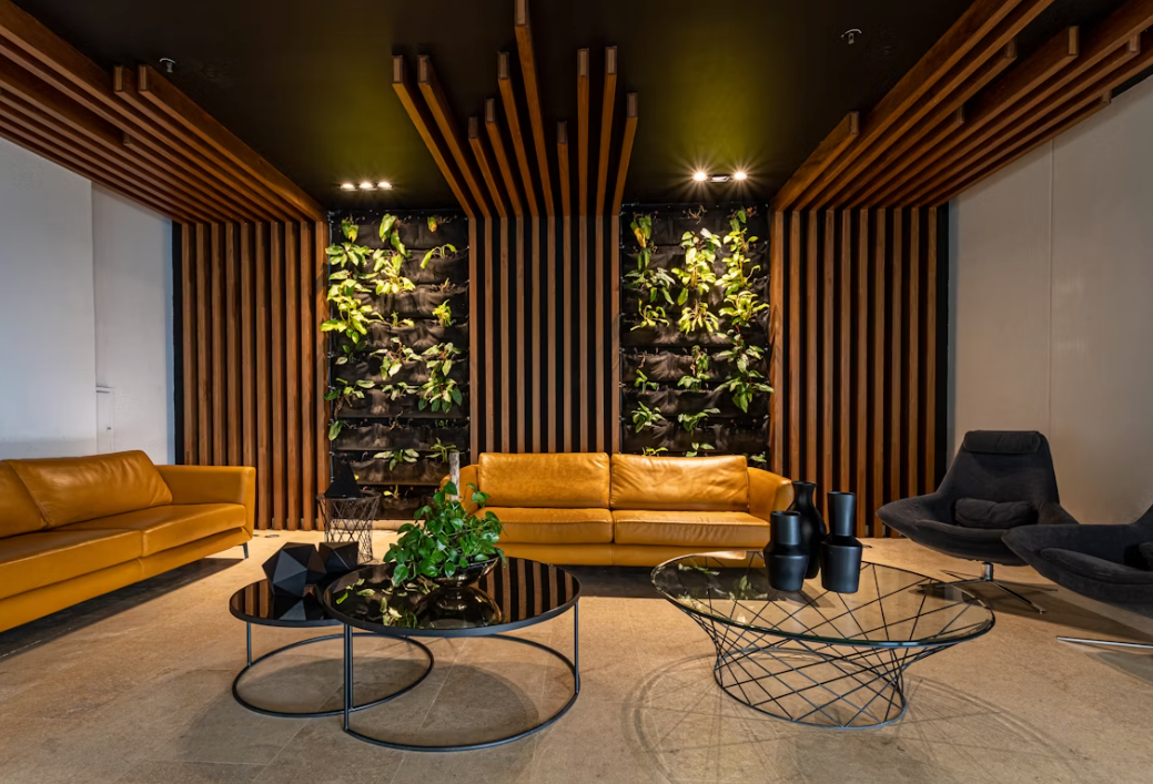 Commercial lounge, tan leather sofas, timber slat walls and ceiling, two planted living wall panels, stone floor.